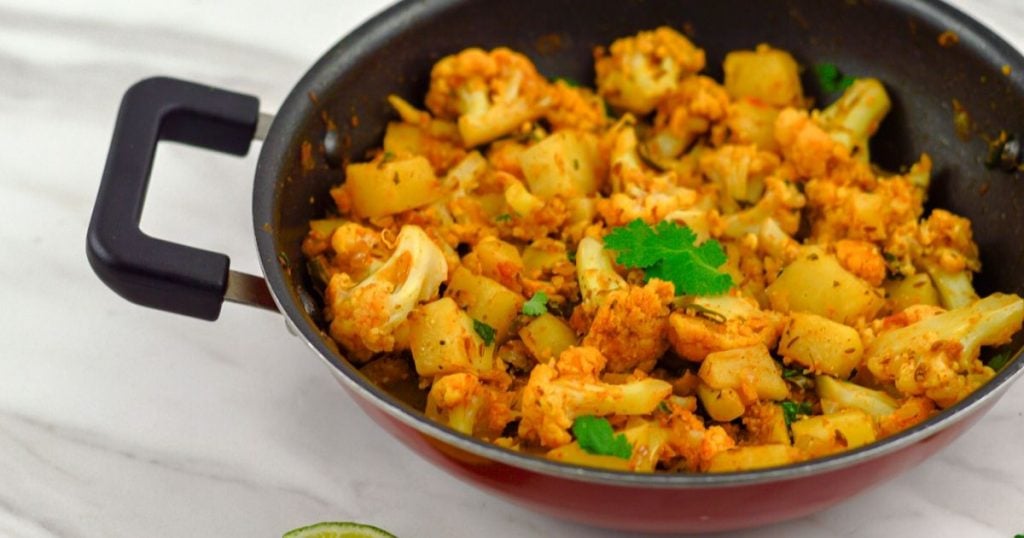 aloo gobi in a black pan placed on white table.