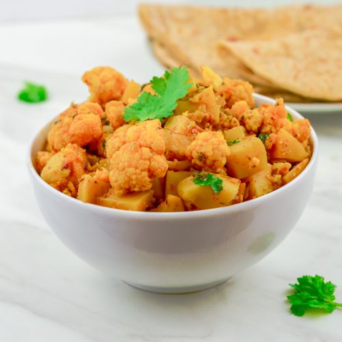 aloo gobi in white bowl with chapatis in a plate on marble background.