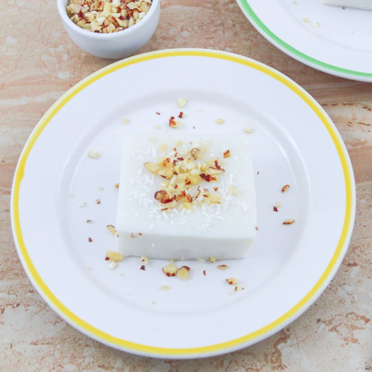 coconut pudding topped with chopped walnuts on plate placed on a table.
