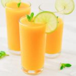 pin image of mango lemonade in 2 full glasses and 1 half glass with mint sprig and lime slice on top on a marble with text saying sparkling mango lemonade.