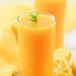 mango lemonade in 2 full glasses with mint sprig on top on a marble.