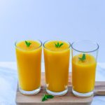 pin image of mango lemonade in 2 full glasses and 1 half glass with mint sprig on top on a wooden board with text saying frozen mango lemonade.