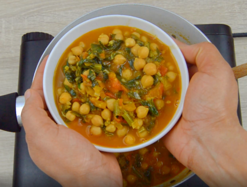 holding a white bowl of chickpea spinach curry.