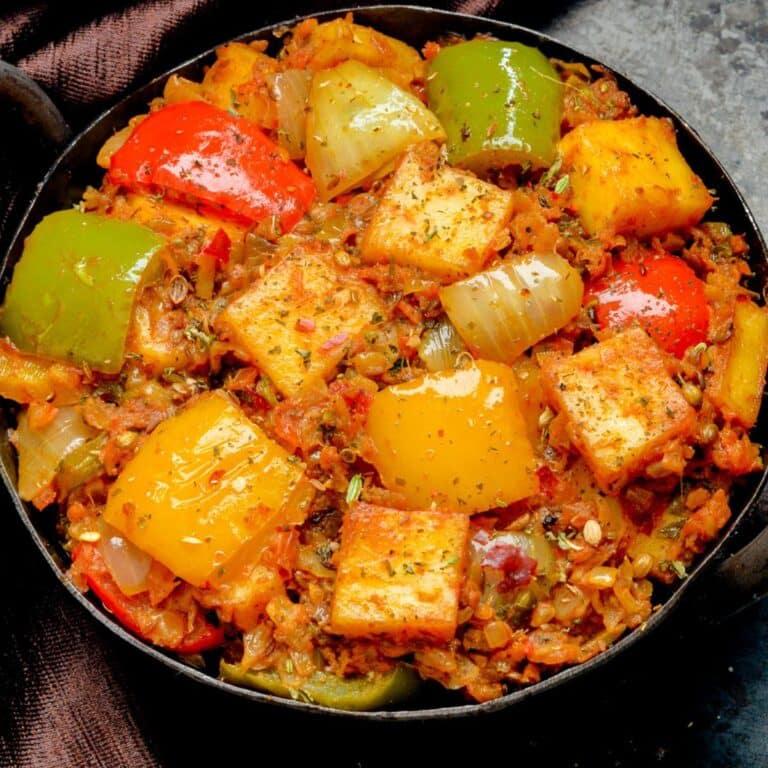 paneer curry with mixed peppers and onion in a kadai placed on a black board along with a brown cloth.