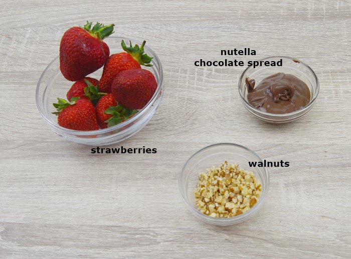 fresh strawberries, chopped walnuts and chocolate spread in individual bowls placed on a table.