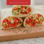 three tortilla wraps filled with vegetables placed on a wooden board with crushed pepper sprinkled on board with cheese tub, bowl of vegetable slices behind and white text overlay on red background.