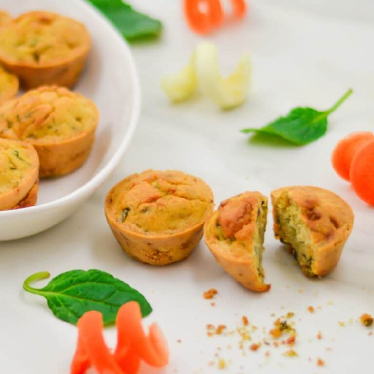 one cut into half and one whole chickpea flour frittatas placed on white table with carrot and zucchini curls.