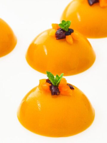 round mango puddings with mint and dry fruit toppings placed on a white plate.