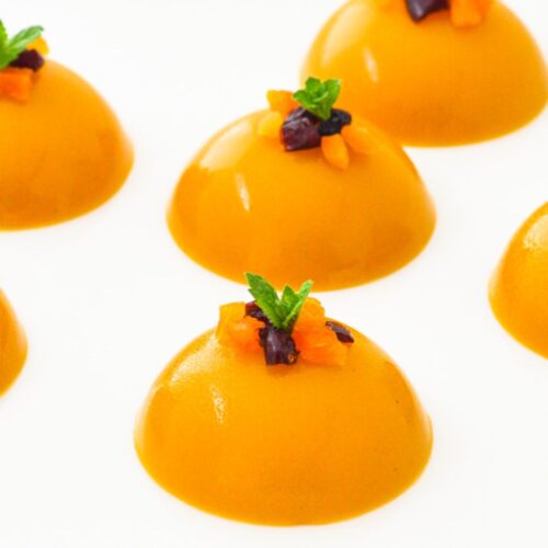 round mango puddings with mint and dry fruit toppings placed on a white plate.