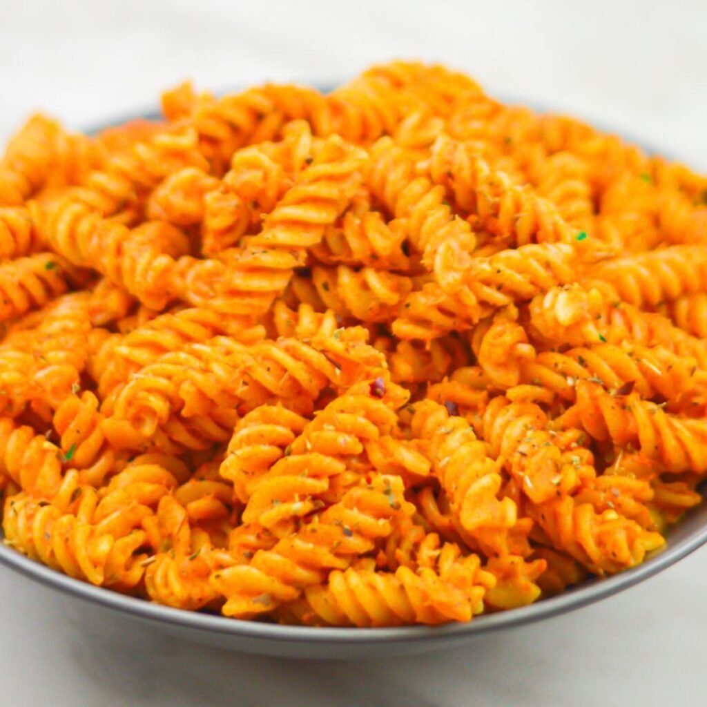 rotini pasta with vegetable sauce in a grey bowl placed on a marble with coriander leaf on side.