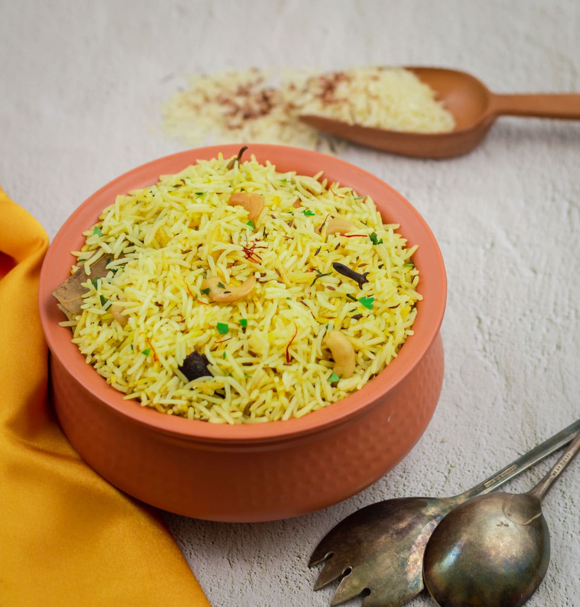 saffron rice in brown pot with orange cloth, spoon, fork and a wooden spatula with raw rice and saffron.