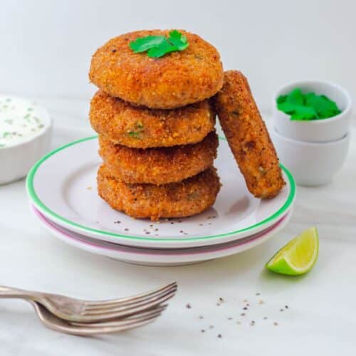 stack of 4 sweet potato patties and 1 patty on side placed on 2 white side plates and yogurt dip bowl and coriander in 2 pinch bowls behind.