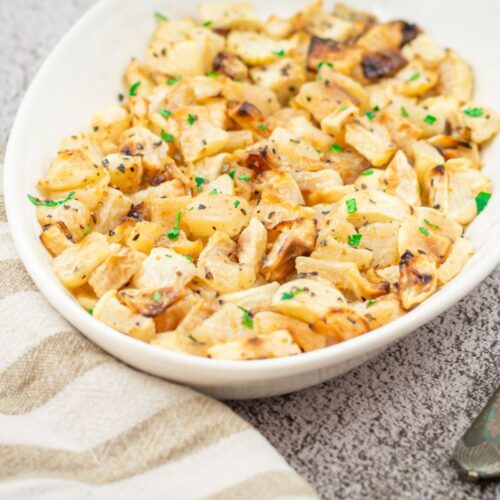 roasted turnips in a white bowl on a granite with a striped cloth and a spoon.