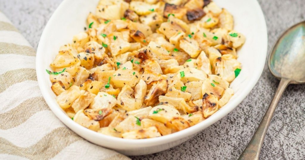roasted turnips in a white bowl on a granite with a striped cloth and a spoon.