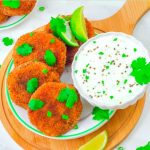 pin image of 4 sweet potato patties in a white side plate with a bowl of yogurt dip on wooden board with text overlay on top.