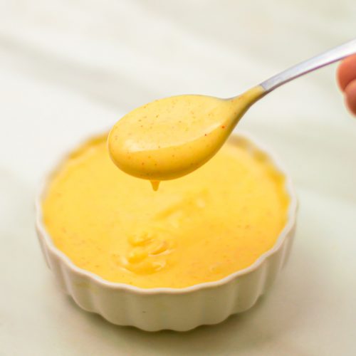 holding a spoon with honey mustard sauce above a white bowl of sauce.
