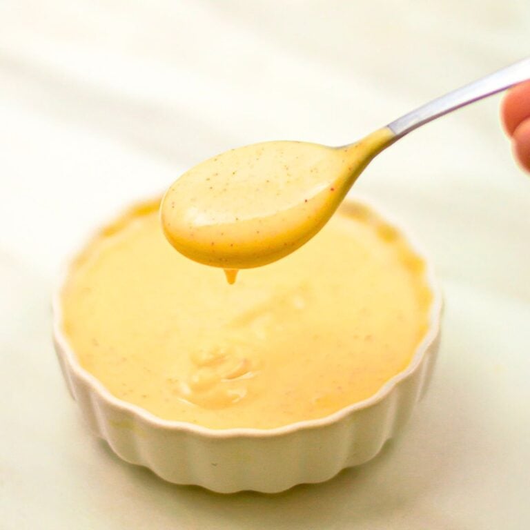 holding a spoon with honey mustard sauce above a white bowl of sauce.
