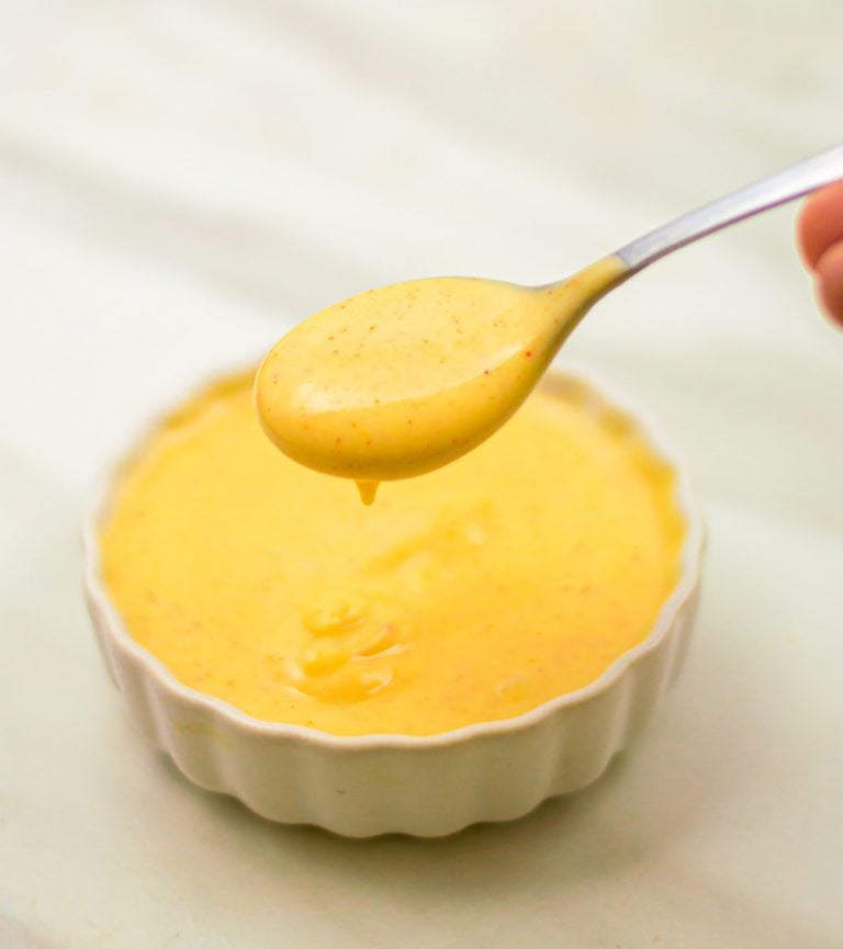 holding a spoon with honey mustard sauce above a white bowl of sauce.