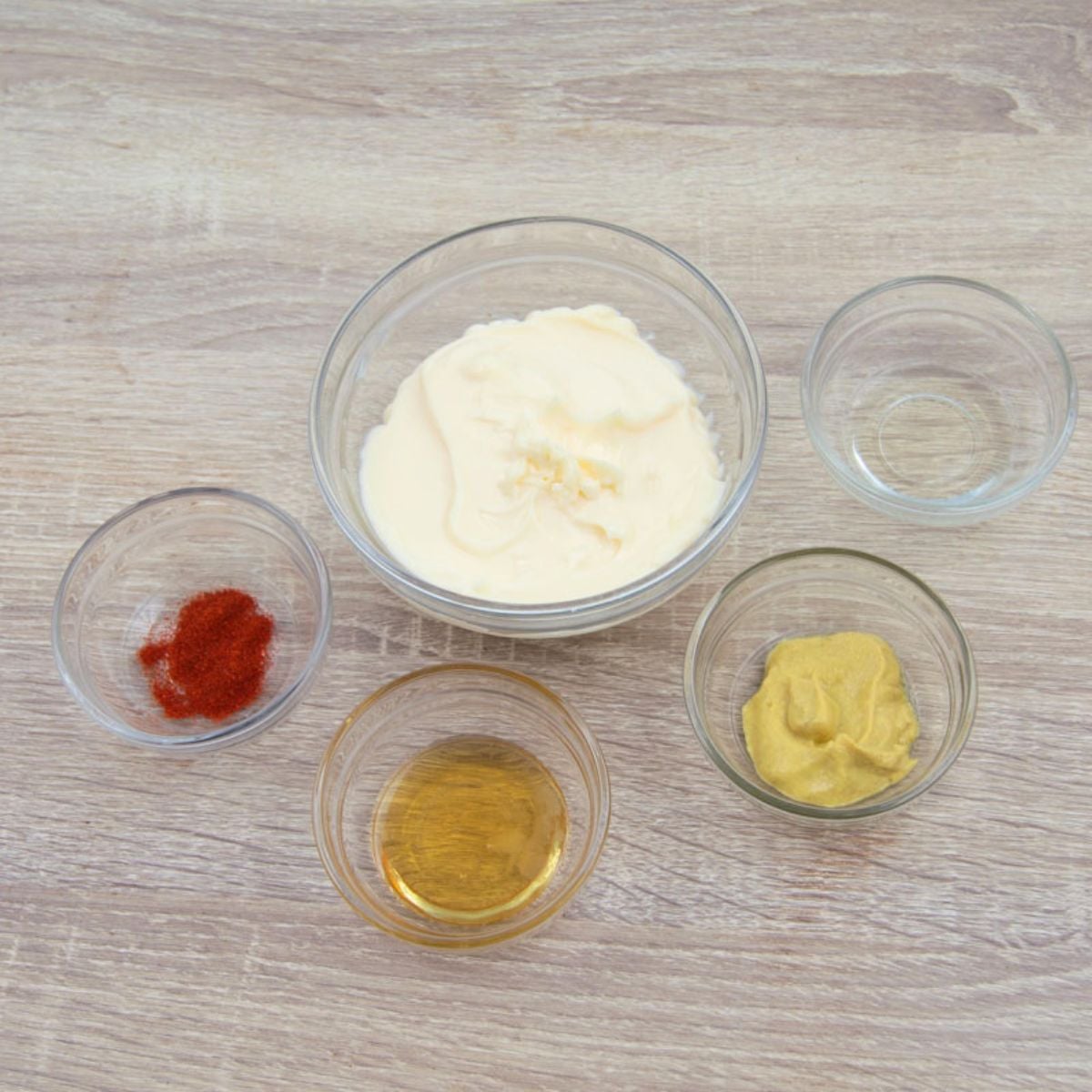 dry and wet ingredients to make honey mustard sauce in individual bowls placed on wooden table.