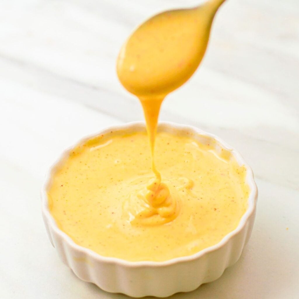 dripping spicy honey mustard sauce from spoon into a white bowl.