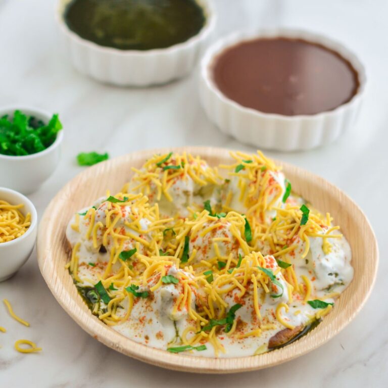 plate of dahi papdi chaat placed on a marble along with two chutneys, sev and coriander leaves.