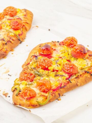2 mini naan bread pizzas placed on a parchment paper on top of a marble.