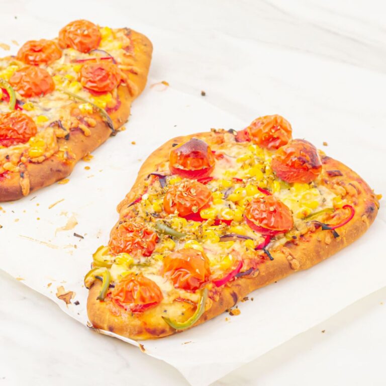 2 mini naan bread pizzas placed on a parchment paper on top of a marble.