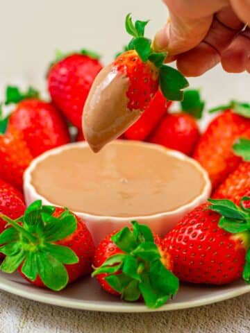 strawberry platter with a white bowl of chocolate dip in the middle placed on a granite background.