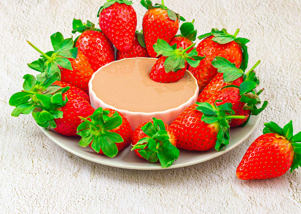 strawberry platter with a white bowl of chocolate dip in the middle placed on a granite background.