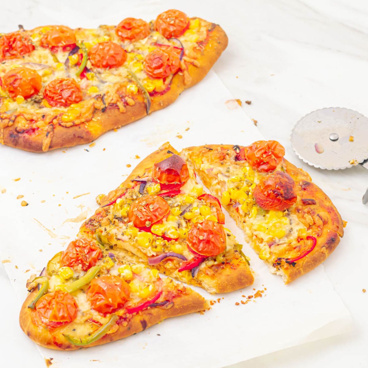 two naan bread pizzas placed on a marble along with a cutter.