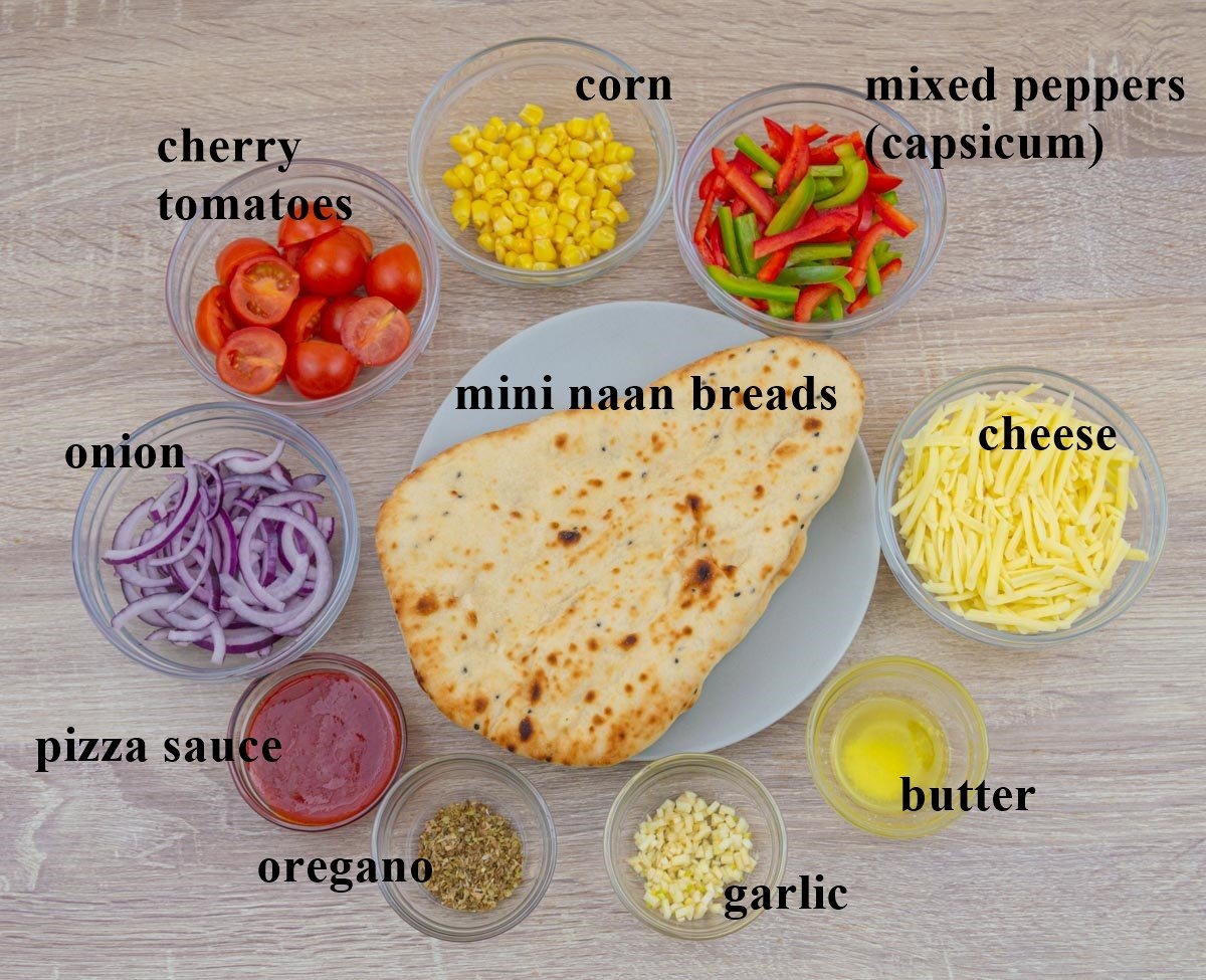 mini naan breads, vegetables, pizza sauce, cheese, oregano, garlic and butter kept in individual bowls placed on a wooden table.