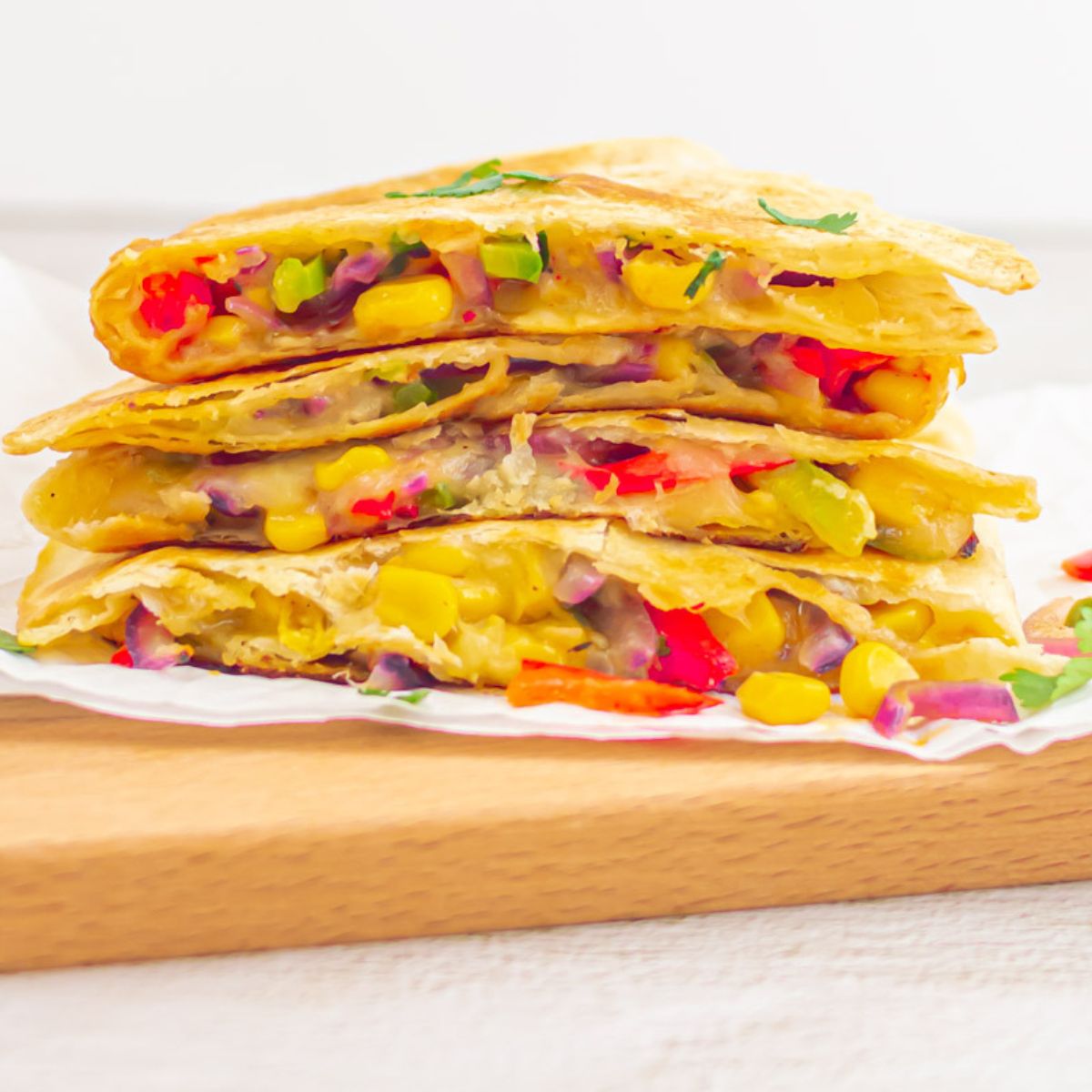 vegetable quesadillas stacked on a baking paper on a wooden board.