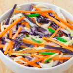 mayo free coleslaw in a white bowl placed on a tile.
