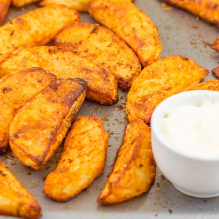 baked potato wedges in a tray with one wedge dipped in a mayo in pinch bowl.