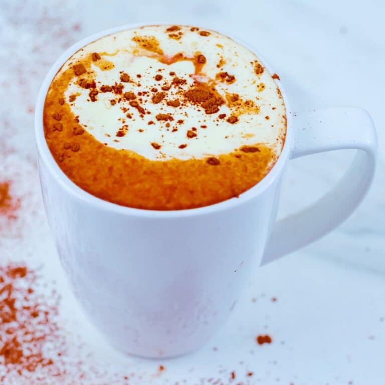 A white mug of homemade hot chocolate topped with whipped cream and sprinkled cocoa powder on a marble.