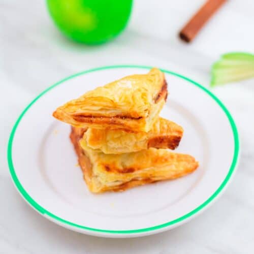 Mini apple turnovers on a plate placed on a marble along with a green apple and cinnamon.