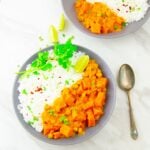 butternut squash curry and rice with corinader and lemon wedge in a grey plate placed on a marble.