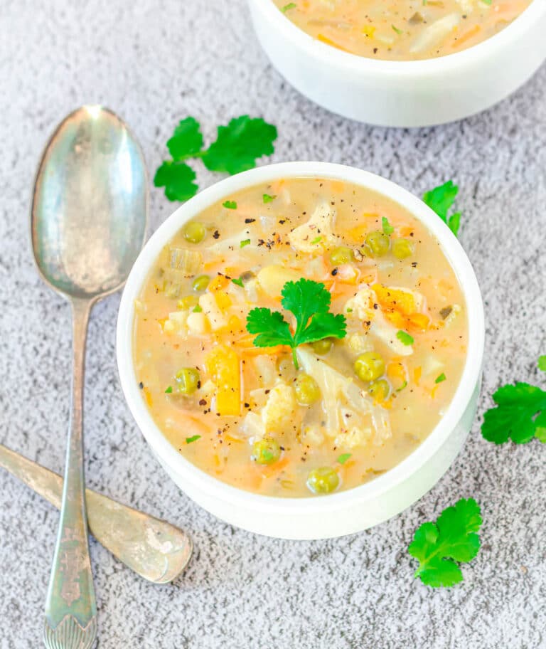 creamy vegetable soup in a white bowl placed on ceramic with a spoon.