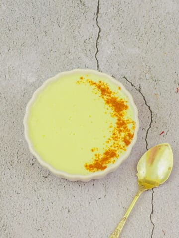 vegan vanilla custard with sprinkled spice powder in a white bowl placed on a tile with a spoon.