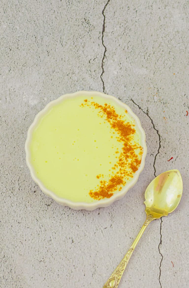 vegan vanilla custard with sprinkled spice powder in a white bowl placed on a tile with a spoon.