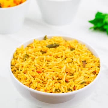 A white bowl of mint pulao placed on a marble along with a bowl o dish and yogurt.f potato