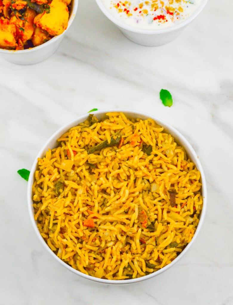 pudina pulao in a white bowl placed on a marble along with a bowl of potato dish and a bowl of yogurt.