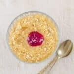 coconut milk rice pudding in a glass bowl placed on a tile with 2 spoons.
