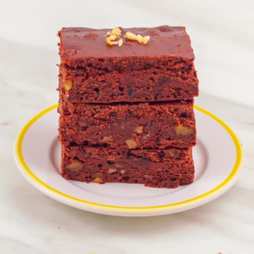 a white plate of stacked walnut brownies placed on a marble.