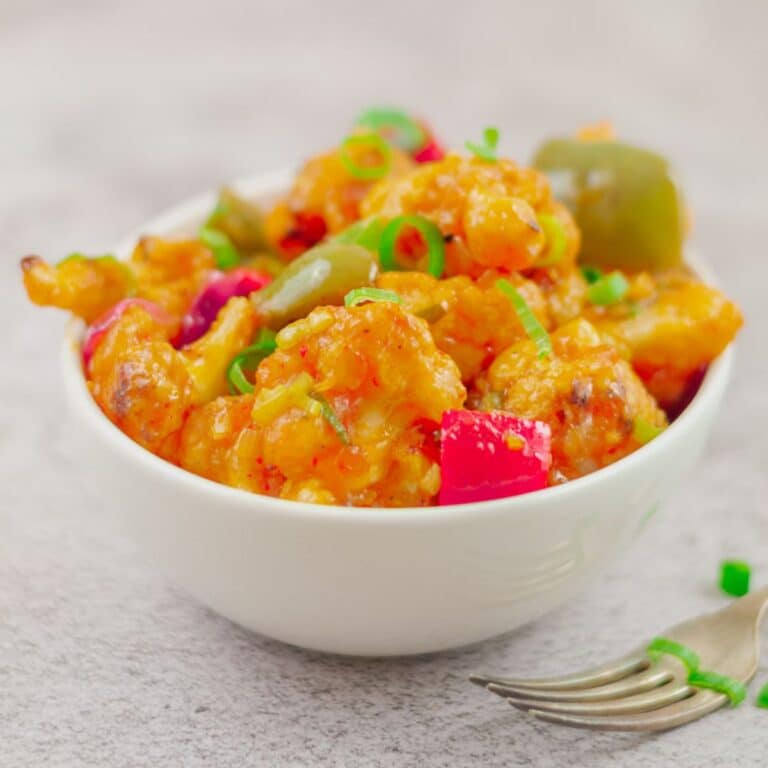 white bowl of gobi manchurian in a white bowl placed o granite with a fork next to it.