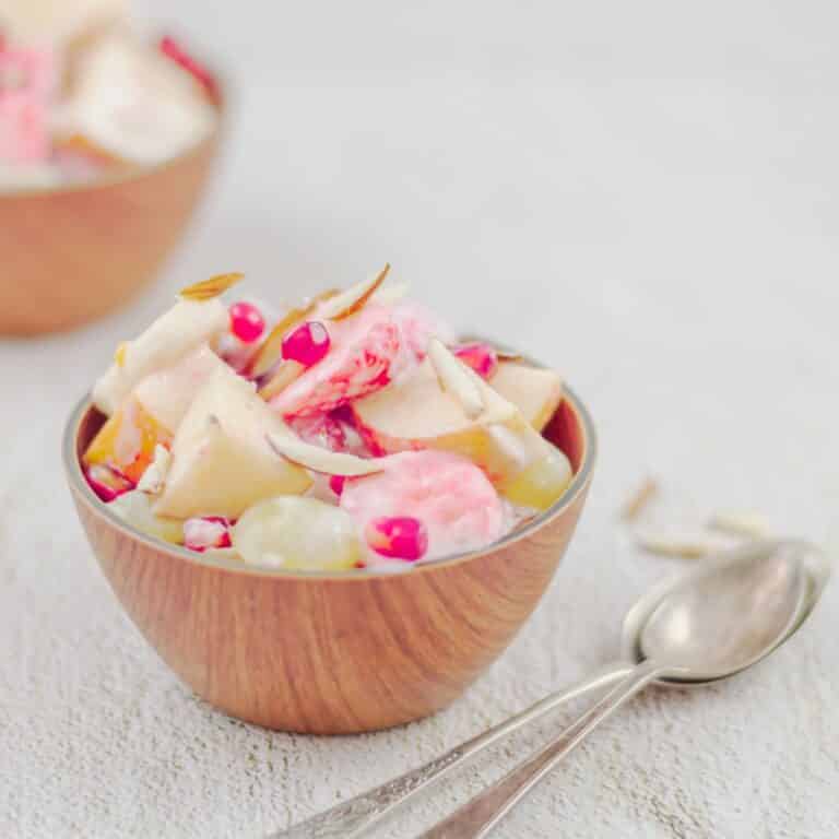 side shot of creamy yogurt fruit salad placed on a tile along with 2 spoons.