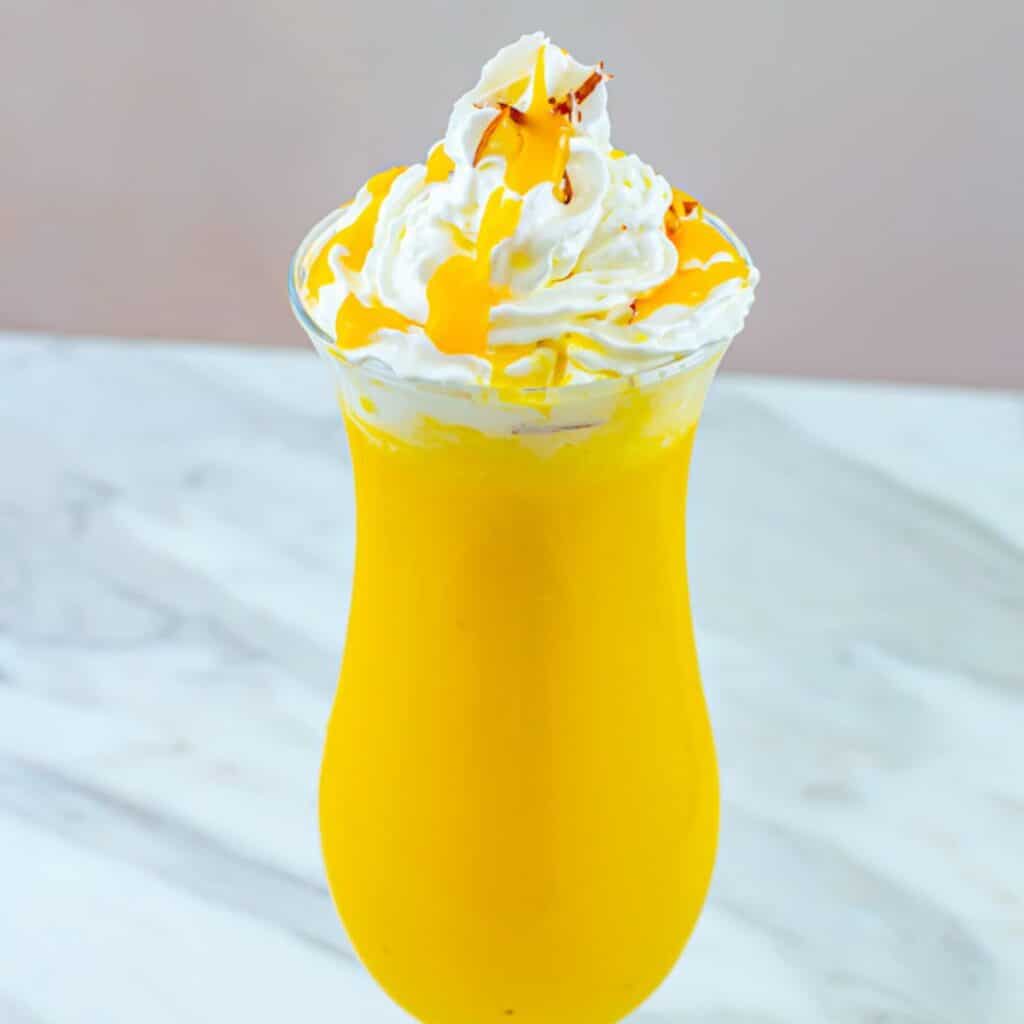 close up shot of mango milkshake in a tall glass topped with whipped cream.
