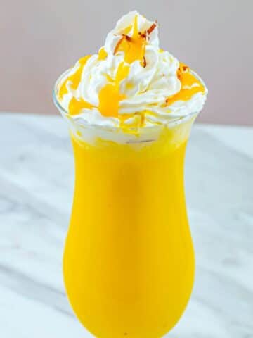 close up shot of mango milkshake in a tall glass topped with whipped cream.