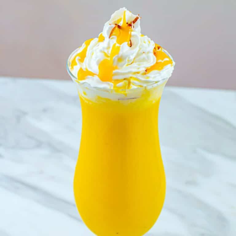 close up shot of mango milkshake in a tall glass topped with whipped cream.