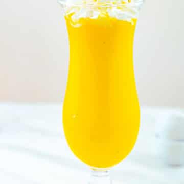 mango milkshake in a tall glass with a whipped cream on top.